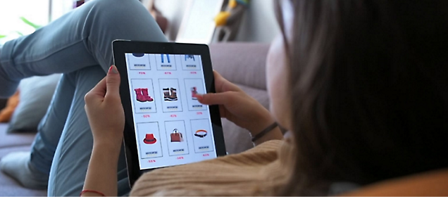 Ein Mädchen, das auf einem Bett liegt und sich eine Einkaufswebsite auf einem Tablet ansieht.