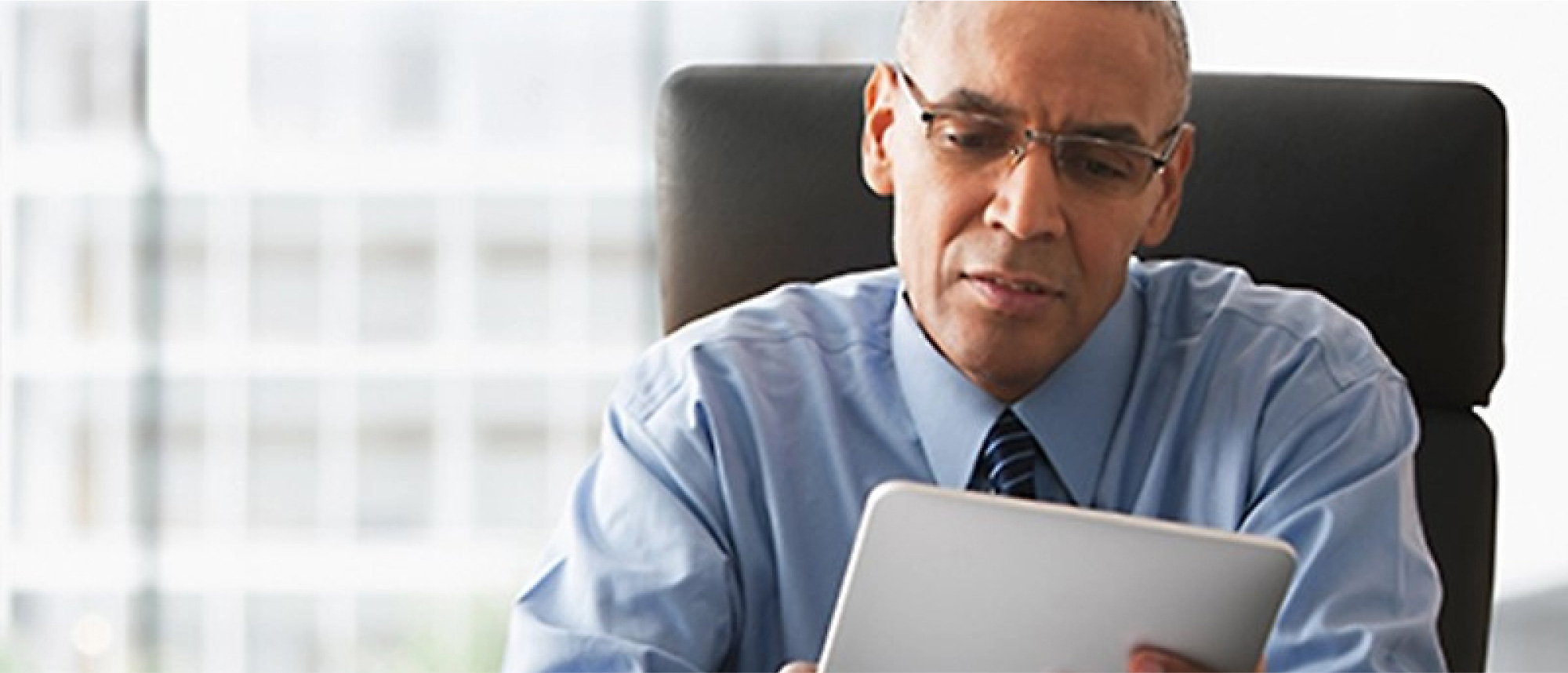 A man sitting in an office looking at a tablet.