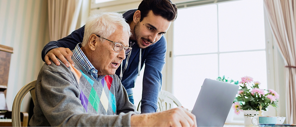 A person looking at a computer and talking with an older individual