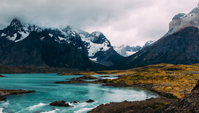 A blue lake in front of mountains partially covered by clouds.