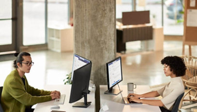 A man and a woman collaborating during a Microsoft Teams meeting while working in an open office setting on dual monitors.