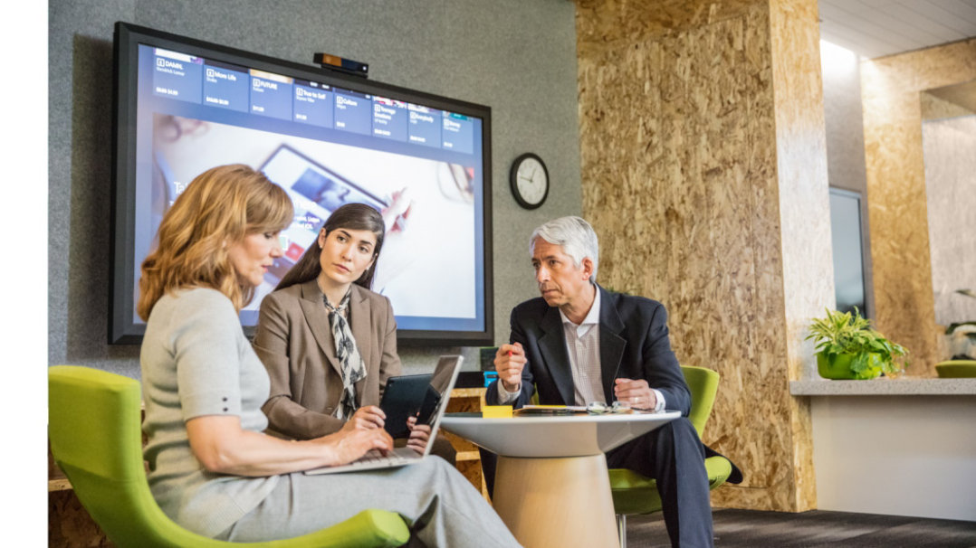 Three businesspeople having a discussion at a small table in an open area.