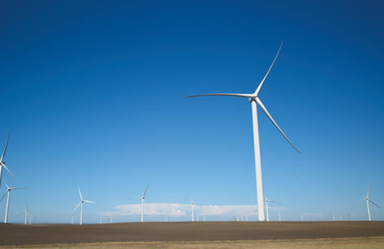 A striking blue sky over a dirt field that is home to a large windfarm.