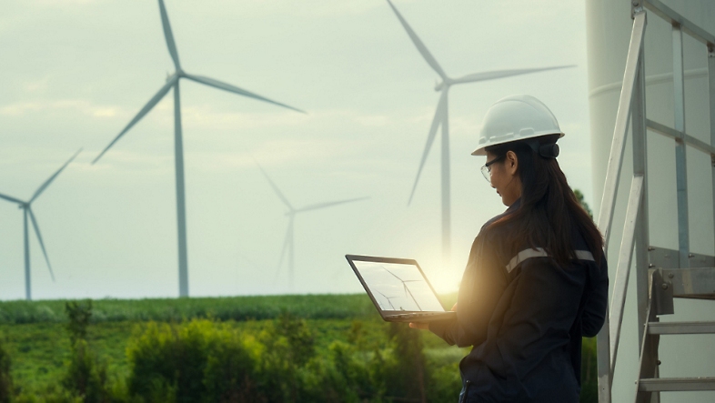 A person holding a laptop standing in a field with turbines.