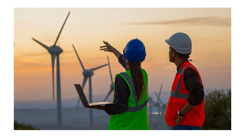 Electrical engineer woman and businessman standing in front of wind turbines discussing technical problems at a wind power plant electric energy station.