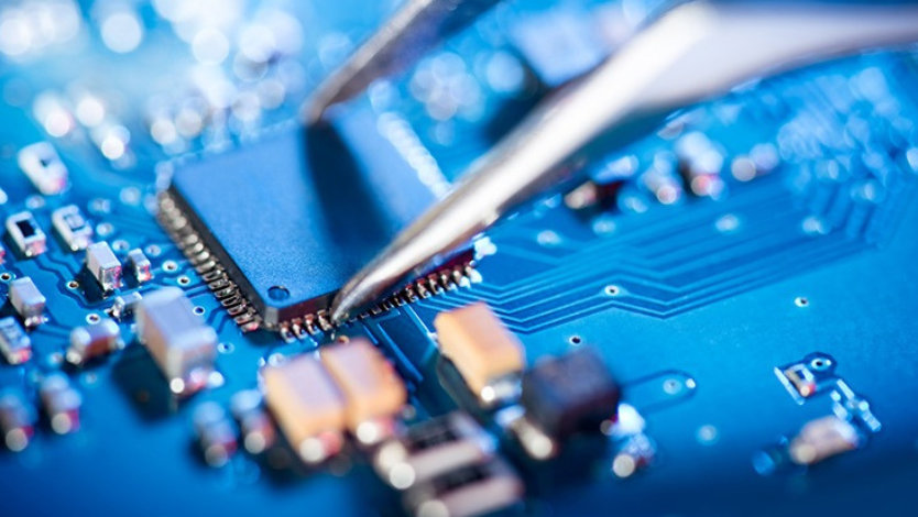 Close-up of an electronic technician holding tweezers and assembling a circuit board.