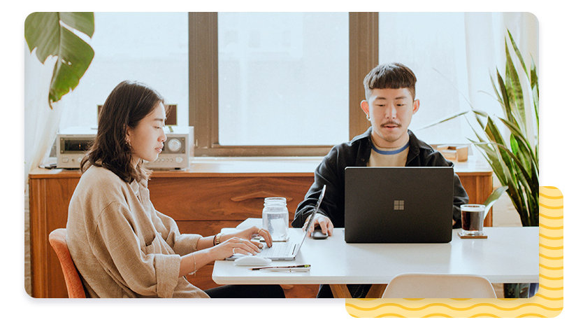 Two people using laptops on large table