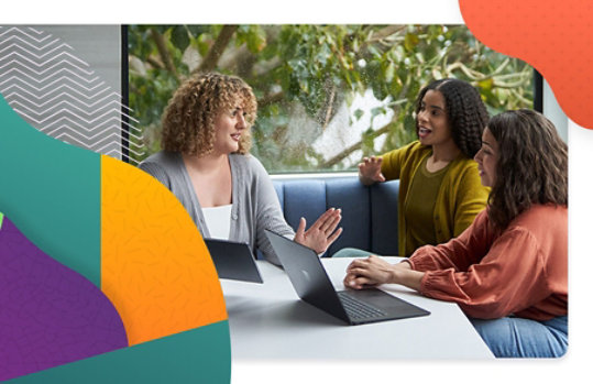 Three coworkers sitting at a table talking and sharing their devices