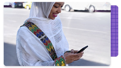 A person wearing a head covering, smiling as they are looking at their mobile phone