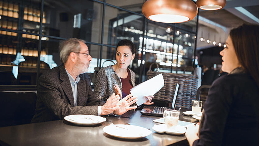 A senior businessman, creative team leader, and female team member having a meeting at a restaurant.