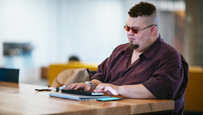 A man who is blind, types on a braille keyboard while also working through a mobile phone.