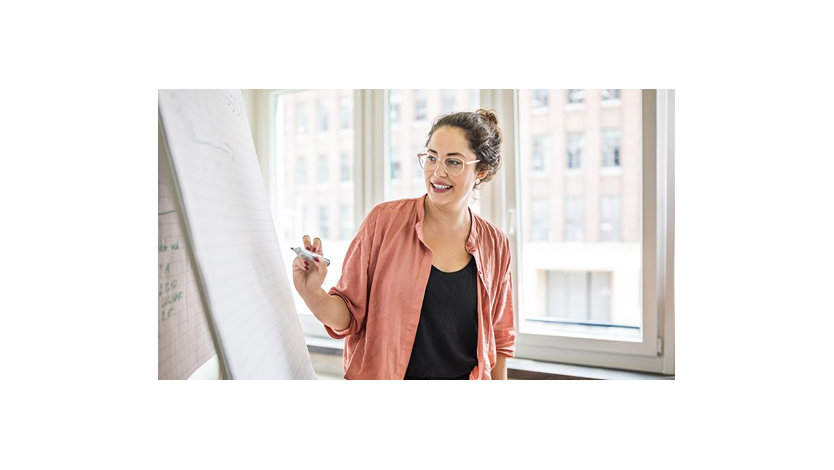 A businesswoman writes on a flip chart while giving a presentation in an office.