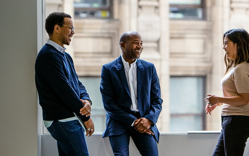 Three coworkers talking happily in an office setting. 