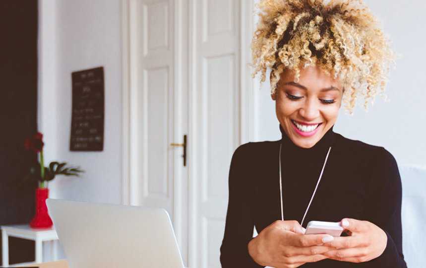 Woman sitting at a desk in a home office using a smart phone.