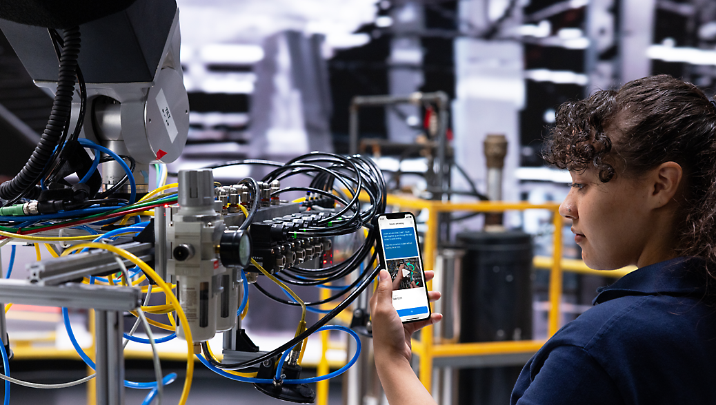 A female technician using a smartphone to adjust or monitor a complex machine with multiple wires and components 