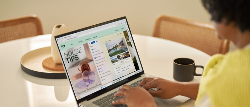 A person in a yellow shirt uses a laptop displaying a website titled "house tips" at a kitchen table