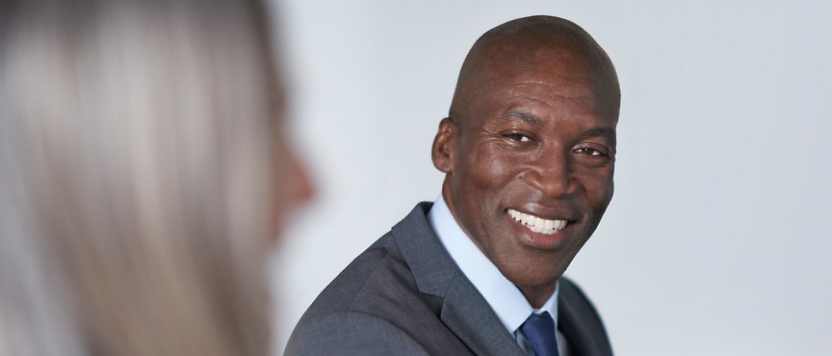 A smiling black man in a business suit facing a woman with blonde hair, both engaging in a professional discussion.