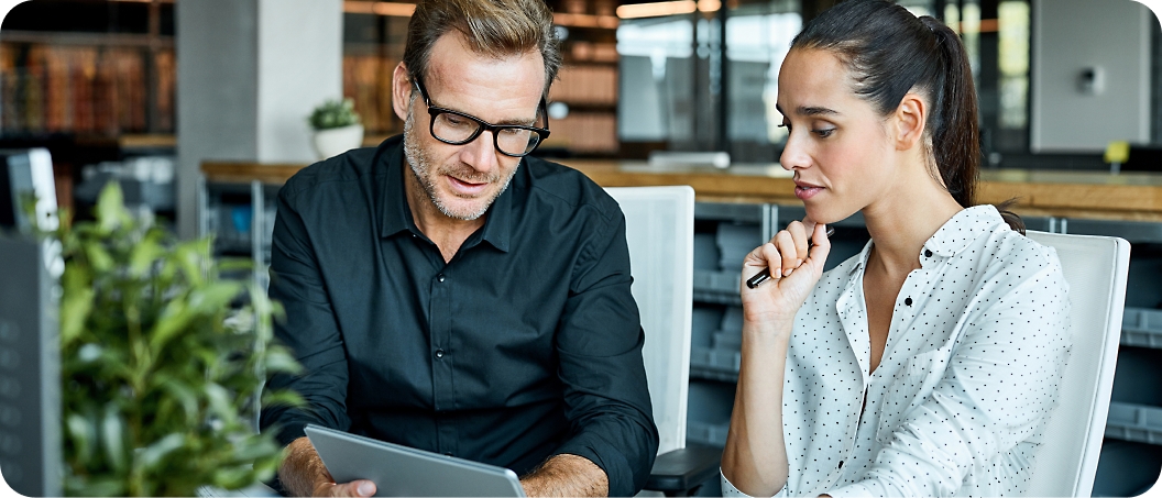 Two people sit in an office setting, looking at a tablet.