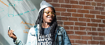 A woman wearing glasses and a hat is standing in front of a whiteboard