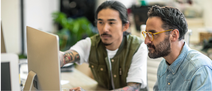 Two men working together at a computer in an office environment.