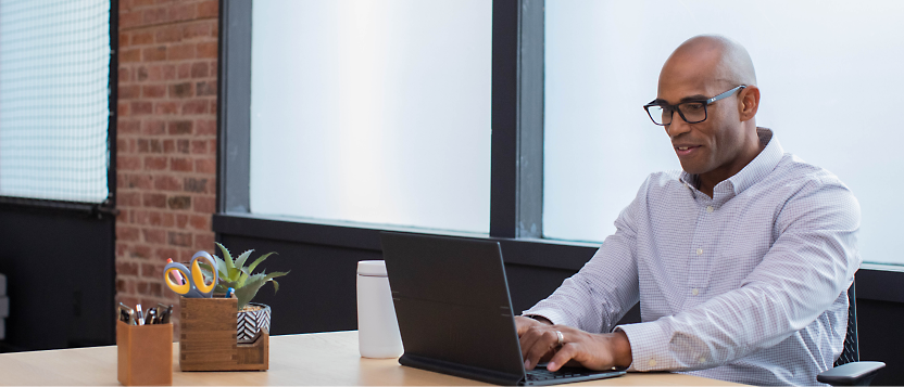 Un homme portant des lunettes et une t-shirt en train de travailler sur un ordinateur portable dans un environnement de bureau moderne.