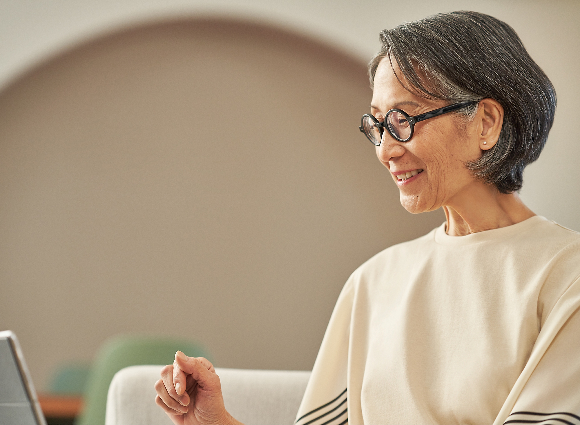 A woman with spectacles smiling and working on her laptop.