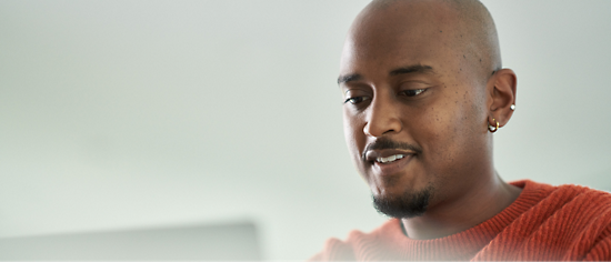 A man in an orange shirt is using a laptop.