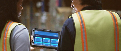 Two people in vests are looking at a tablet