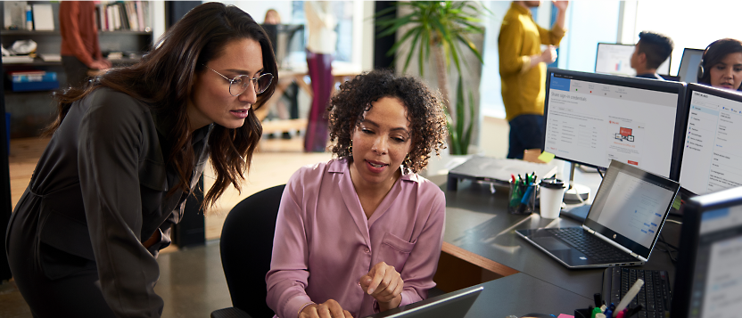 Two women collaborating at a computer in an office environment.