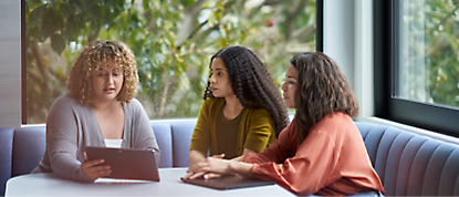 Three women sitting at a table with a tablet.