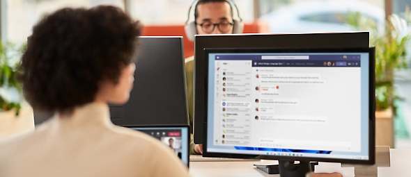 Женщина взаимодействует в рамках собрания Microsoft Teams, одновременно работая в открытой среде Office на двойном мониторе
