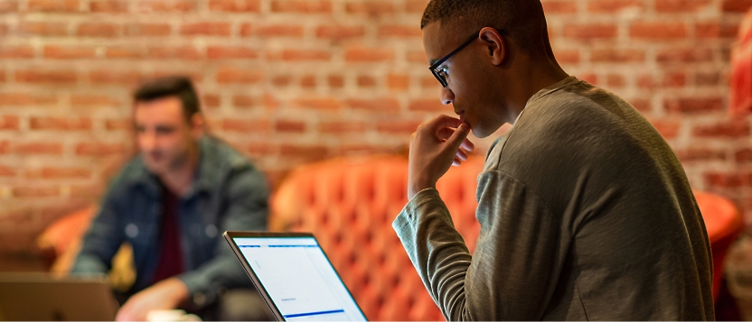 Man working on a laptop in the foreground, with another person on a laptop in the background.