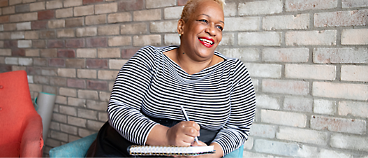 A person smiling while holding a pen and notebook