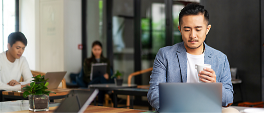 A person in a suit is using a computer, with two other individuals working on their laptops in the background