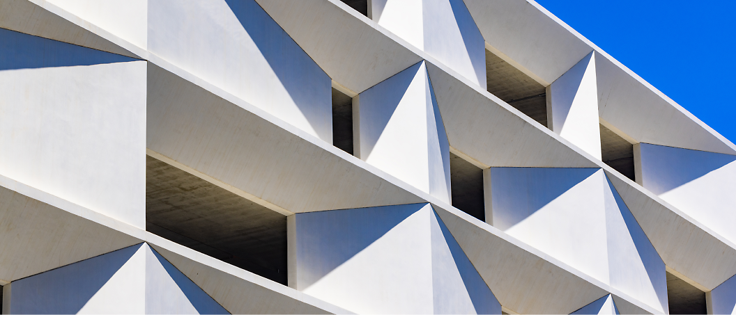 Vue abstraite d’un bâtiment moderne avec une façade blanche en béton géométrique sous un ciel bleu clair.