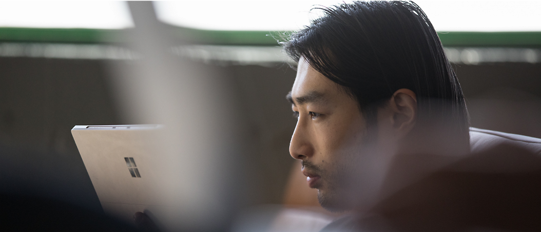 Man with long hair using a tablet, focusing intently in a softly lit indoor setting.