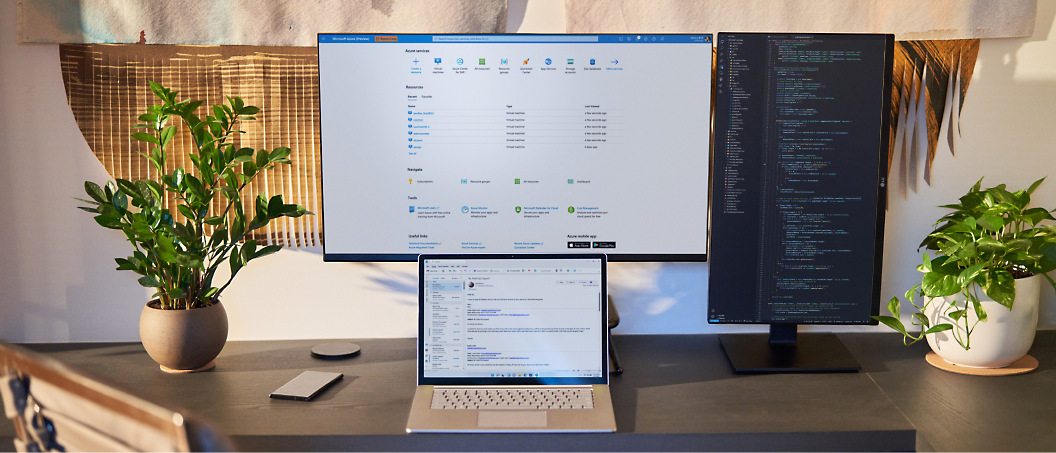 A home office setup with two monitors displaying code and data, a laptop open in front, and plants on either side of the desk.