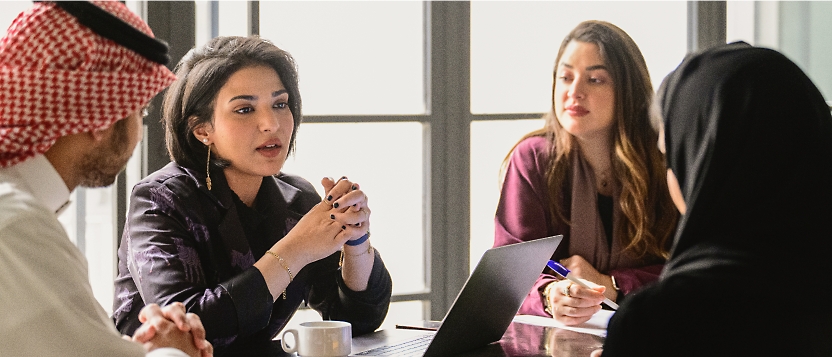 A group of four people, three women and one man, are having a serious discussion at a table.