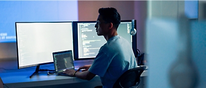 A man sitting at a desk with two monitors and a laptop 