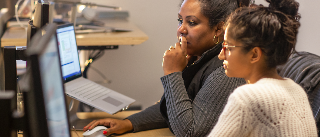 Deux femmes concentrées sur un écran d’ordinateur dans un bureau moderne.