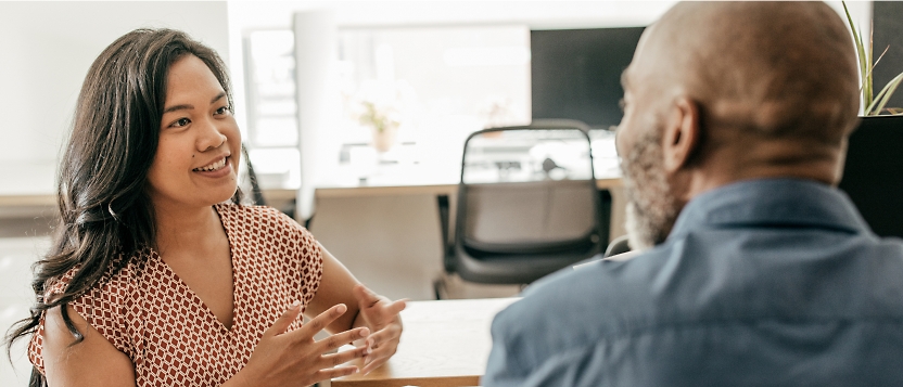 Two people are having a conversation at a table in an office setting. The person on the left is speaking,