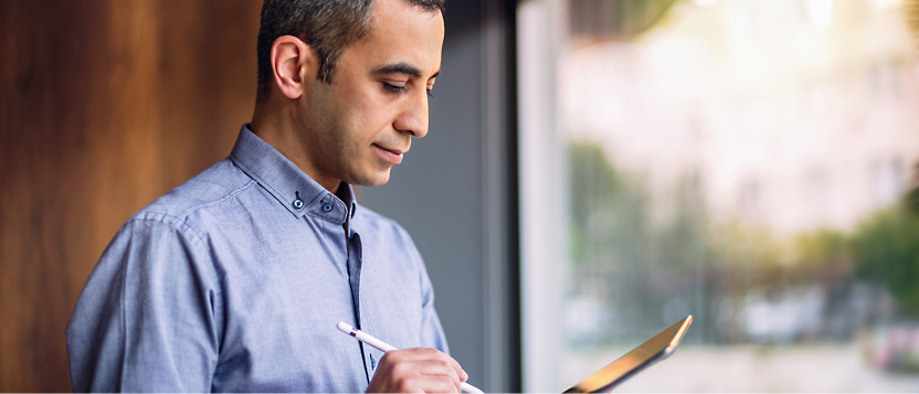 Man writing on clipboard near a window.