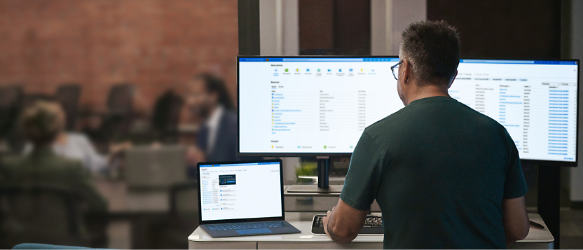 A person working on a computer with a spreadsheet open, with blurred colleagues in the background.