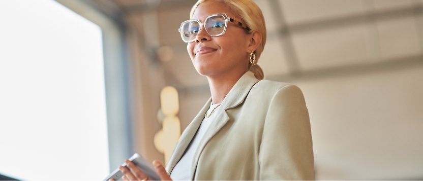 Una empresaria con gafas sostiene un teléfono móvil.