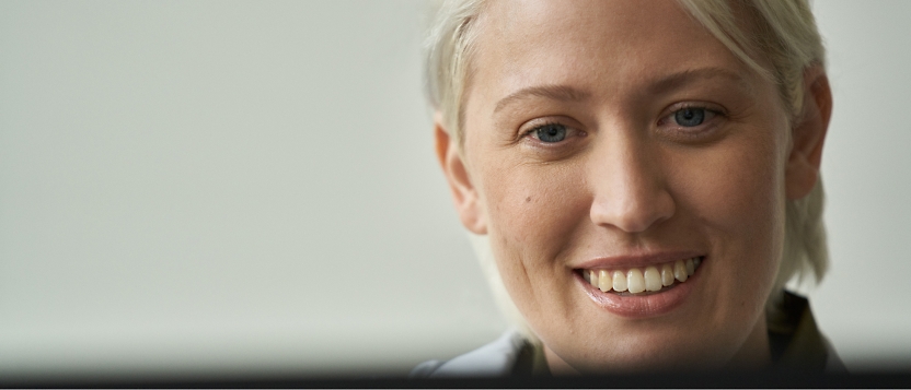 A woman is smiling in front of a computer screen.