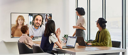 A group of people sitting at a table watching a video conference.