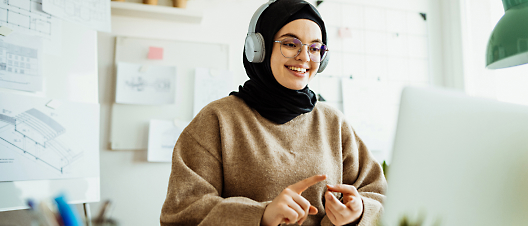 Woman with headphones working on a laptop in a bright office setting.