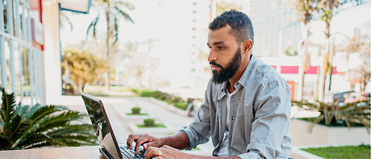 Man working on a laptop at an outdoor table in an urban setting.