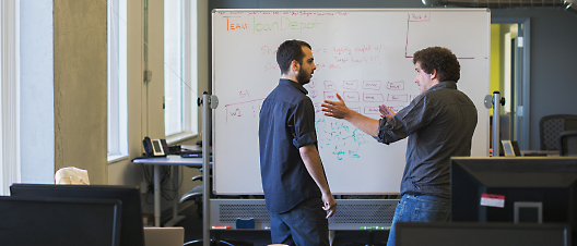 A person standing in front of a whiteboard discussing with another person