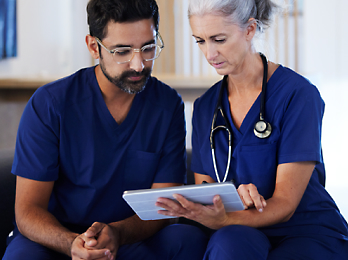 A person and another individual, both wearing blue scrubs, looking at a tablet